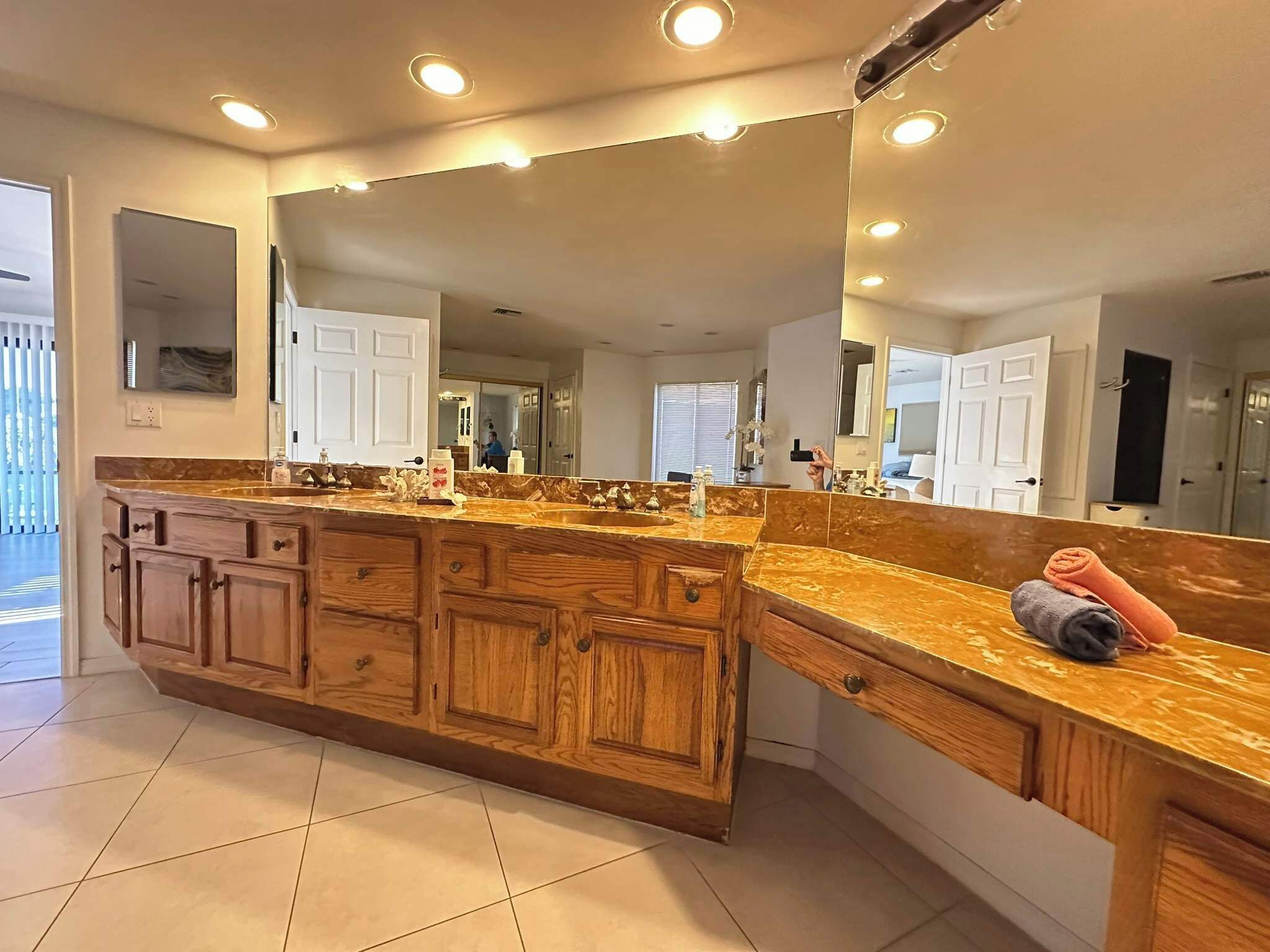 A bathroom with a wooden vanity, a large mirror, and a tiled floor.