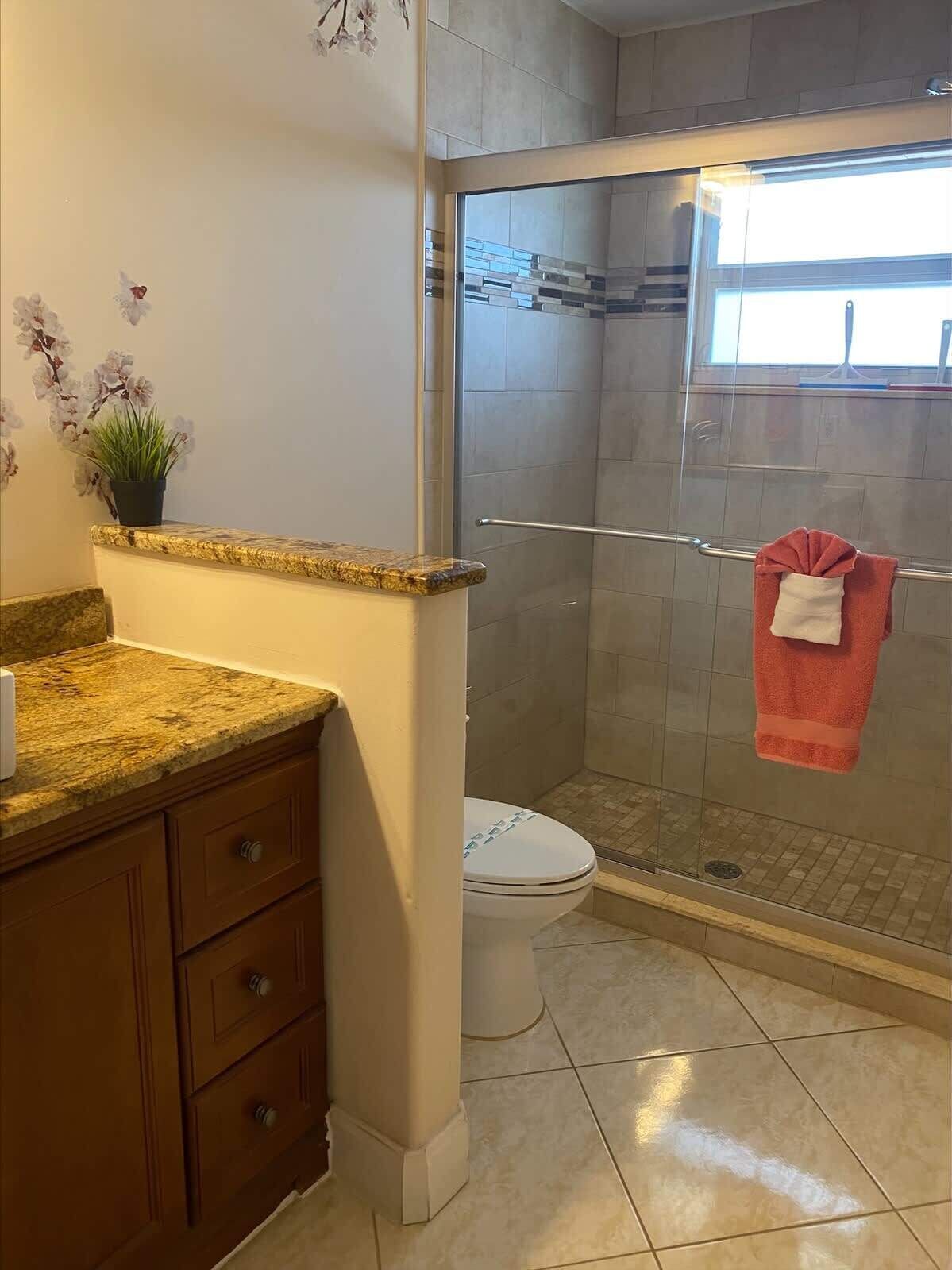 A bathroom with a granite countertop, a toilet, a glass shower enclosure, and a towel rack with a towel.