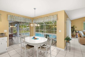 A dining area with a white table and chairs, a view of a swimming pool, and a kitchen area with a counter and cabinets. - Villa Seastar - Cape Coral (Cape Coral)