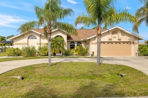 A single-story house with a garage, surrounded by a well-maintained lawn and palm trees. - Villa Seastar - Cape Coral (Cape Coral)