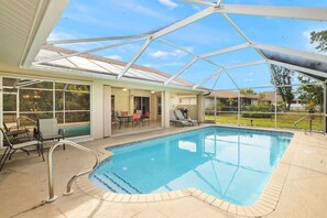 A covered swimming pool with a glass ceiling, adjacent lounge area with chairs, and a view of the surrounding landscape. - Villa Seastar - Cape Coral (Cape Coral)