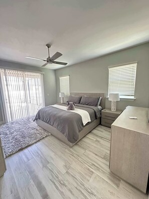 A bedroom with a bed, a desk, a chair, a ceiling fan, and two windows with blinds. - Villa Crystal Breeze (Cape Coral)