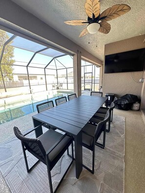 A covered outdoor dining area with a pool view, a ceiling fan, and a mounted TV. - Villa Crystal Breeze (Cape Coral)