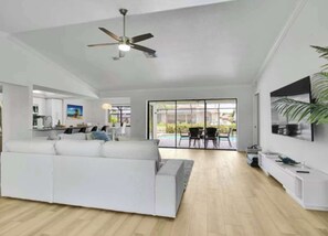 Ein großzügiger Wohnbereich mit weißem Sofa, Deckenventilator und Blick auf eine Terrasse.