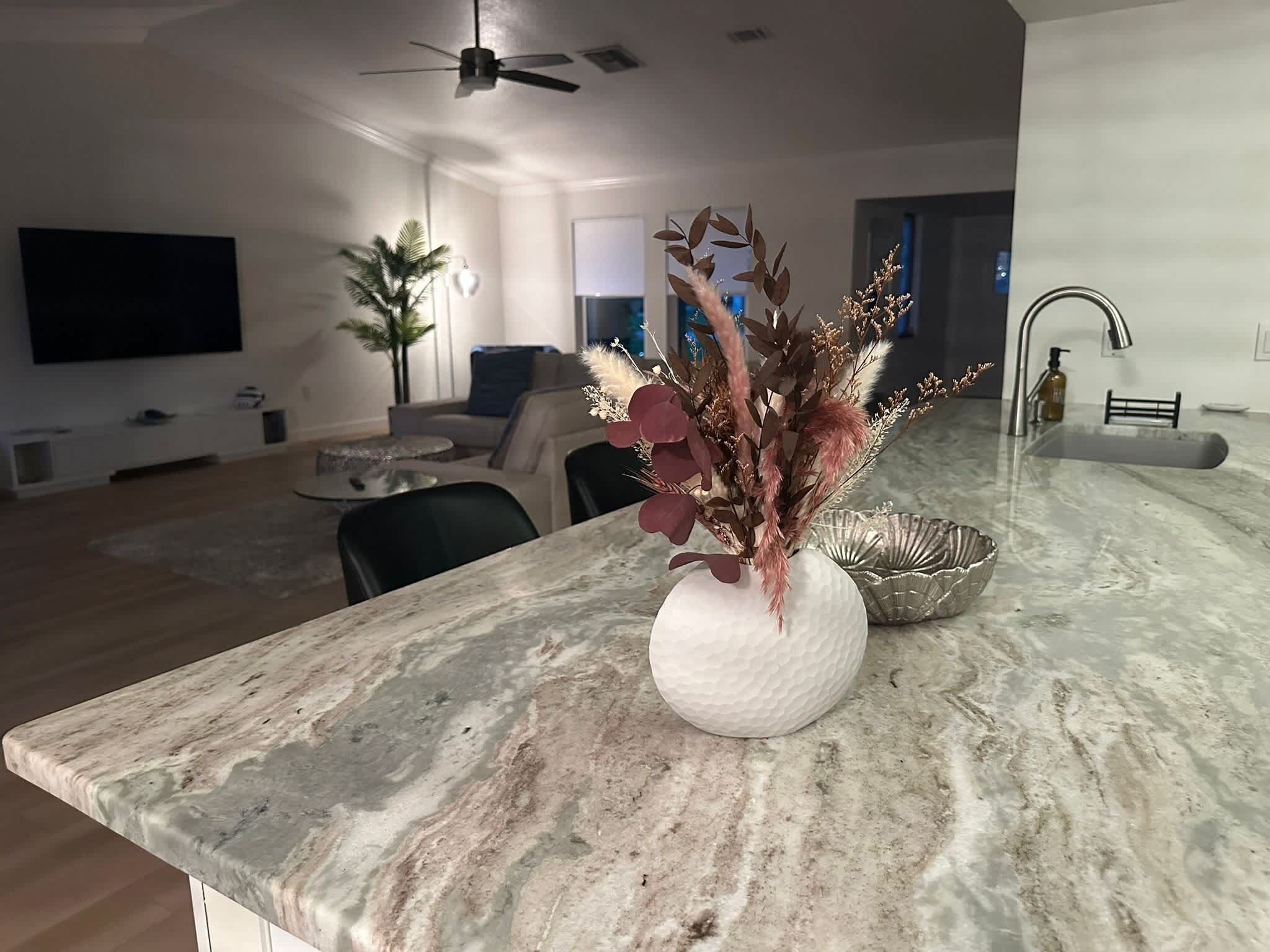 A modern kitchen with a marble countertop, a vase with dried flowers, and a sink with a soap dispenser.