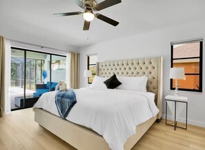Ein Schlafzimmer mit einem großen Bett, einem Deckenventilator, einem Fenster mit Vorhängen und einem kleinen Tisch mit einer Lampe.