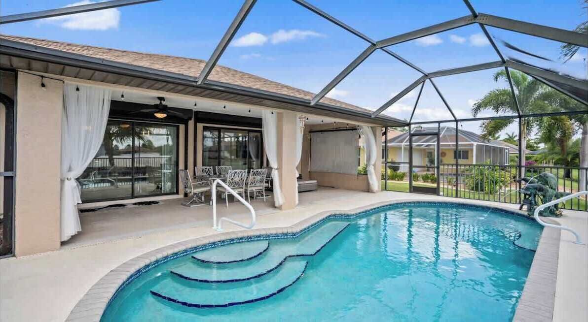 En swimmingpool med tagdækning, en terrasse med stole og udsigt til et boligområde.