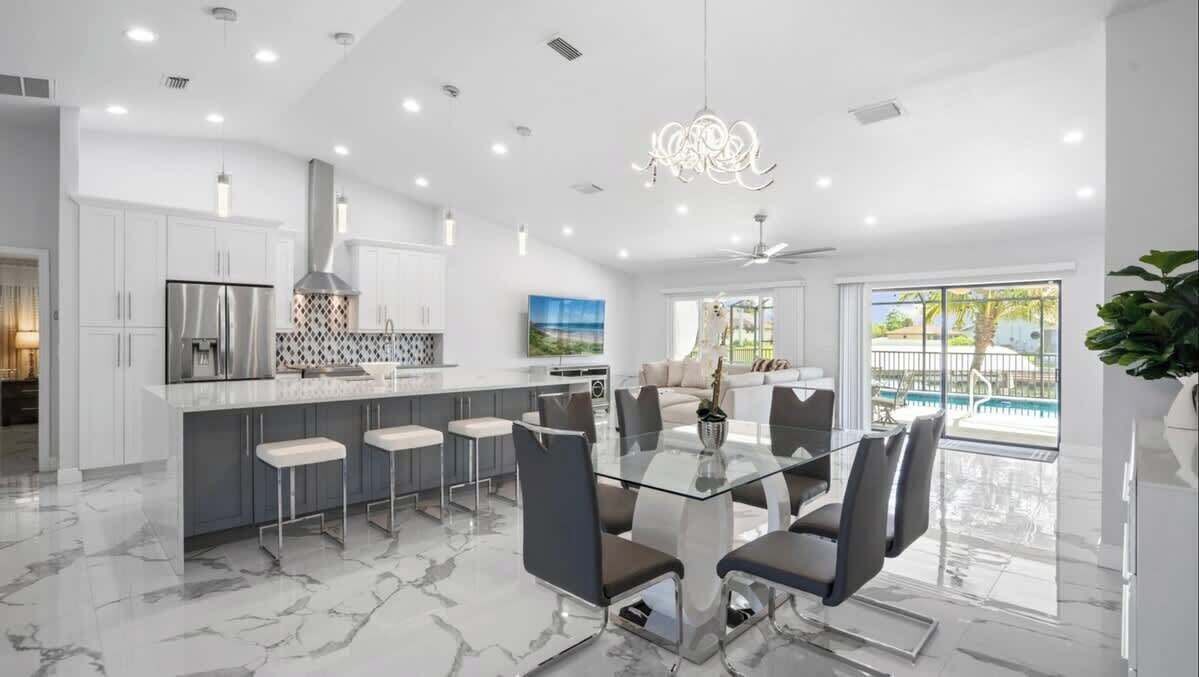 A modern kitchen with white cabinets, a marble floor, and a glass dining table with chairs.