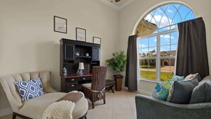Una sala de estar con un sofá, un sillón y un aparador de madera oscura. Se aprecia una ventana grande con vistas a un jardín.