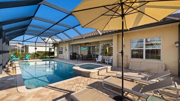 Una piscina exterior cubierta con sillas de descanso y sombrillas, rodeada por un patio con zona de barbacoa.