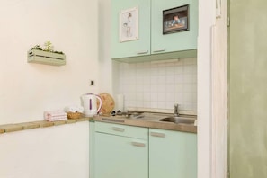 A kitchen with light green cabinets, a white tiled backsplash, a sink, and a small plant on the wall. - Villa Split Art - Pistacio apt (Split)