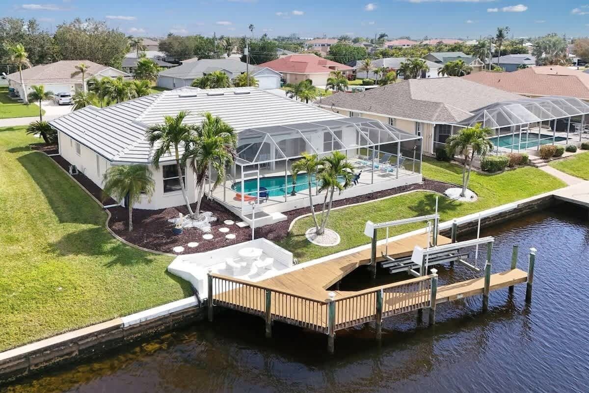 A residential property with a swimming pool, covered outdoor seating area, and a dock extending into a body of water.