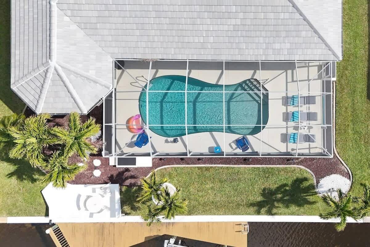 Vista aérea de una piscina con sombrilla, sillas de descanso y palmeras.