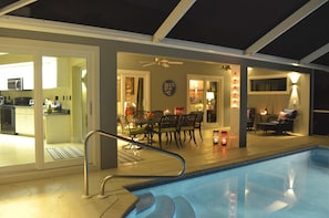 Ein Poolbereich mit Esstisch und Stühlen, einem Deckenventilator und einer durchgehenden Tür erkennbaren Küche.