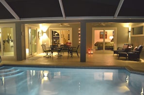 Ein Poolbereich im Freien mit Esstisch und Stühlen, einem Deckenventilator und einem gut beleuchteten Innenraum.