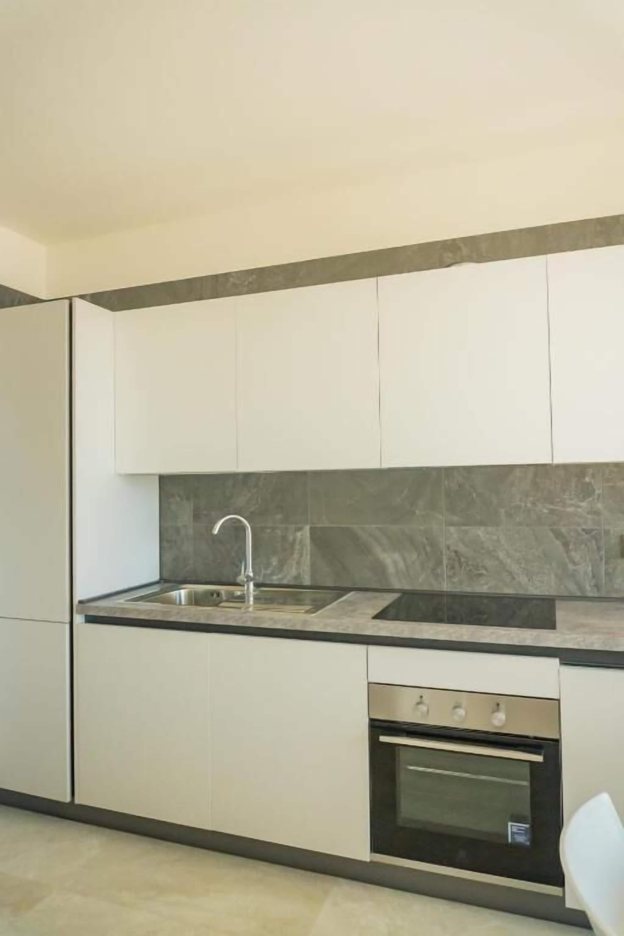 A modern kitchen with white cabinets, a stainless steel sink, a built-in oven, and a marble backsplash.