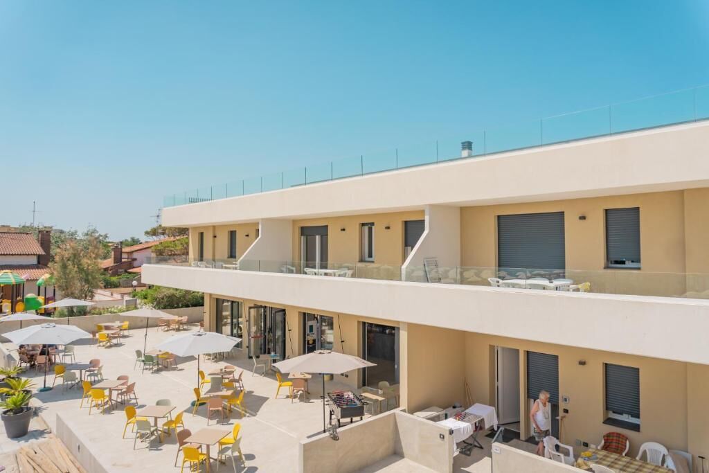 Un hotel con terraza al aire libre, balcón en el segundo piso y cielo despejado.