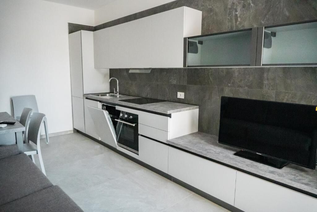 A modern kitchen with white cabinetry, a built-in oven, a sink, and a flat-screen TV.