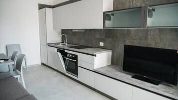 A modern kitchen with white cabinetry, a built-in oven, a sink, and a flat-screen TV.