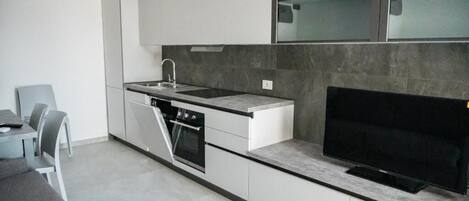 A modern kitchen with white cabinetry, a built-in oven, a sink, and a flat-screen TV.