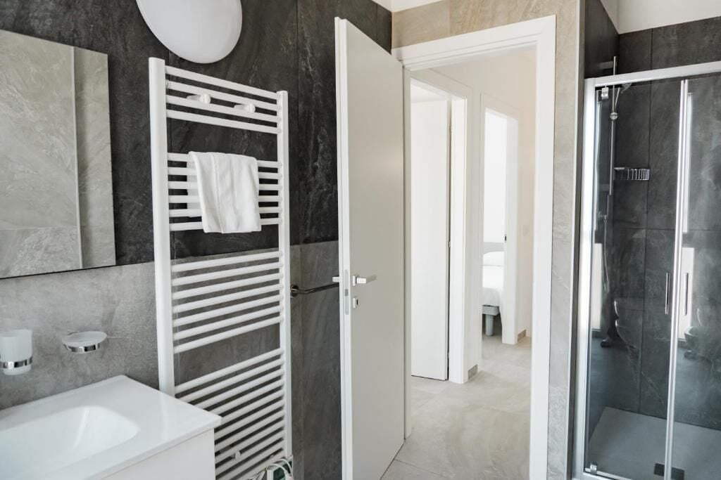 A modern bathroom with a white sink, a towel rack, a glass shower enclosure, and a door leading to another room.