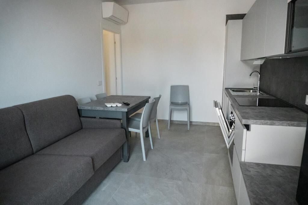 A compact kitchen with a dining area, a grey sofa, and a small table with chairs.