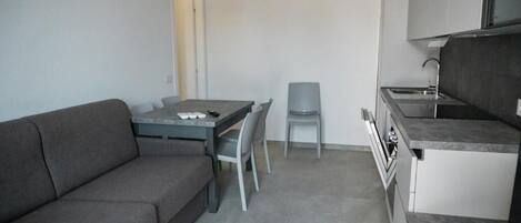 A compact kitchen with a dining area, a grey sofa, and a small table with chairs.