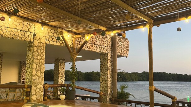 A pool area with a stone wall backdrop, wooden deck, and a view of a lake. - Casa Barú  (Cartagena)