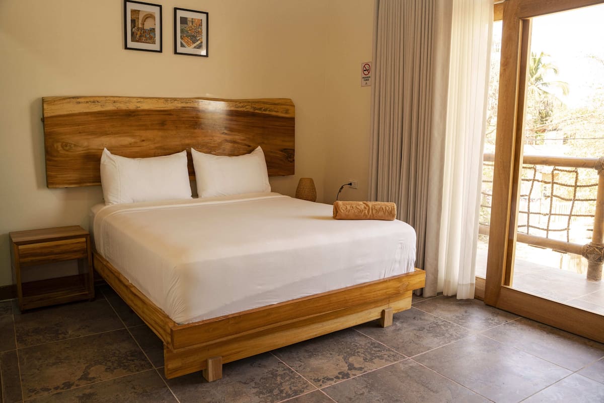 A bed with a wooden headboard, a nightstand, a small table, and a view of the outdoors through a glass door.