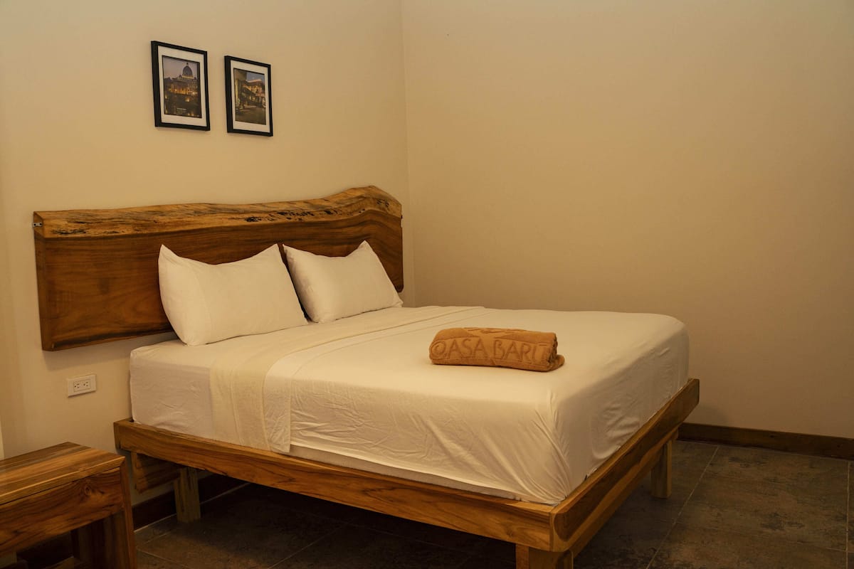 A bed with a wooden headboard, white bedding, and a rolled towel.