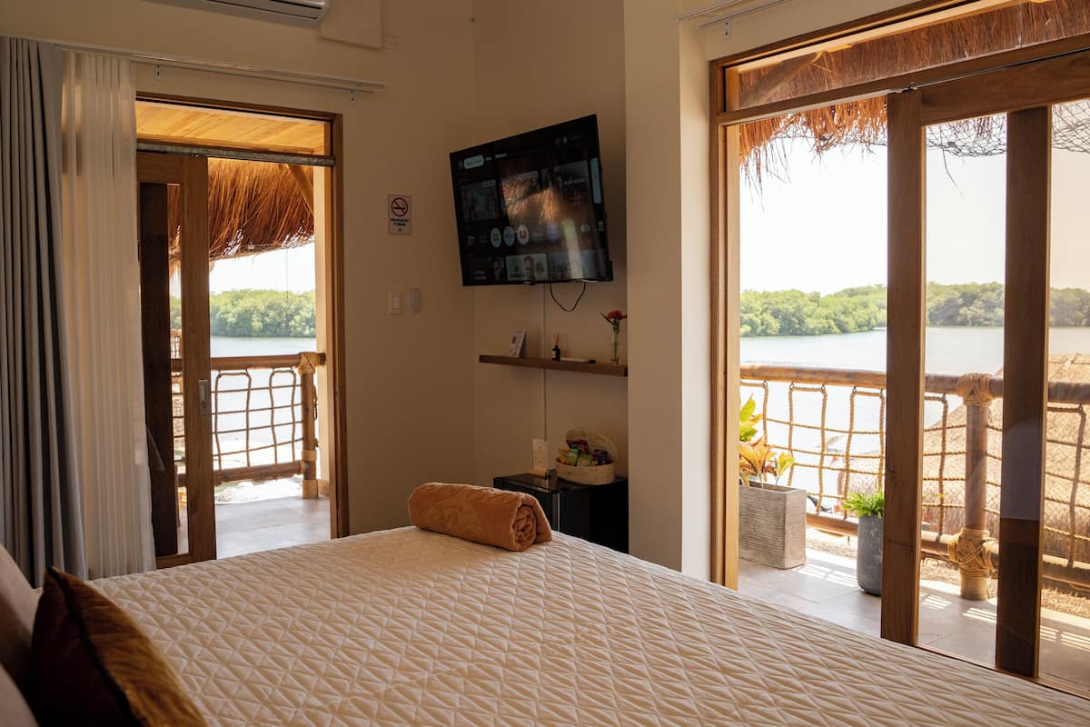 A bedroom with a large bed, a TV, and a view of a lake.