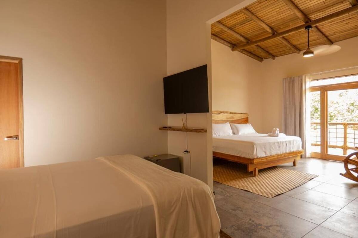 A bedroom with two beds, a TV, a wooden ceiling, and a balcony with a view.