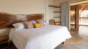 A bedroom with a large bed, a wooden headboard, a bedside table, a chair, and a view of the outside. - Casa Barú  (Cartagena)