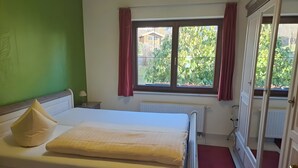 Ein Schlafzimmer mit Bett, Heizkörper, einem Fenster mit Vorhängen und einem Spiegel.
