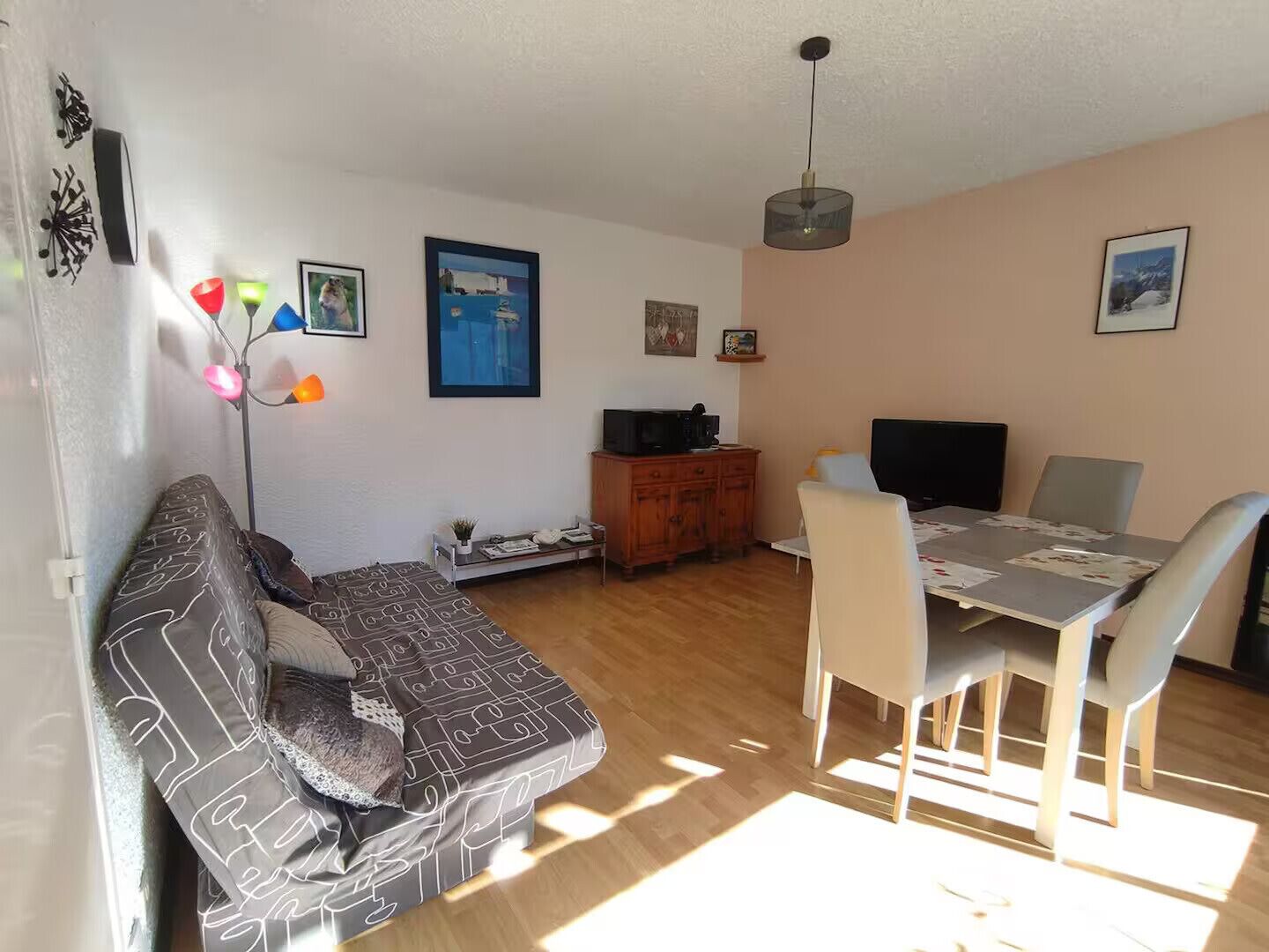 A living room with a sofa, dining table, and chairs. There is a television on a wooden cabinet.