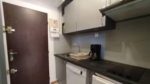 Eine kleine Küche mit dunkler Arbeitsplatte, einer Kaffeemaschine, einem Geschirrspüler und einem Schrank.