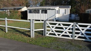 A mobile home with a fenced yard, a small shed, and a white picket fence. - Mobile Home “Lurielle” with Shared Pool, Communal Terrace, and Private Garden (Blonville-sur-Mer)