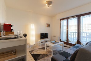 A living room with a sofa, a coffee table, a TV, and a dining area with a table and chairs. - Apartment with Sea View in Villers-sur-Mer (Villers-sur-Mer)