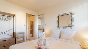 Una camera d'albergo con un letto rifatto, un comò in legno, uno specchio e un bagno visibile attraverso una porta aperta.