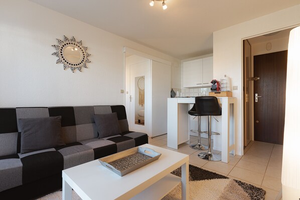 A modern living room with a sofa, a coffee table, and a kitchen area in the background. - Apartment with Sea View in Villers-sur-Mer (Villers-sur-Mer)