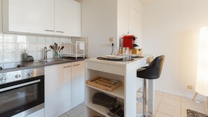Una cucina moderna con mobili bianchi, forno a incasso, macchina da caffè e uno sgabello da bar.