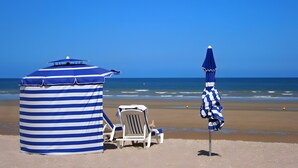Una playa con una sombrilla rayada, una silla de playa y una pequeña estructura.