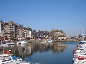 Un port où des bateaux sont amarrés, un ciel dégagé et des bâtiments qui bordent la promenade.