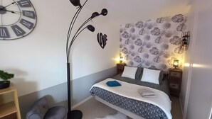 Un dormitorio con cama, lámpara de pie, reloj de pared, planta y papel tapiz estampado.