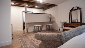 Une pièce avec un plafond en bois, un grand miroir, un bureau, deux tabourets et un tapis à motifs.