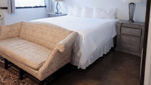 Une chambre d’hôtel avec un lit, un canapé, une table de chevet, une lampe et une fenêtre avec des rideaux.