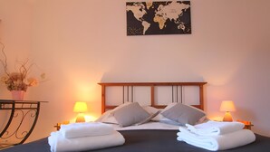 A neatly made bed with pillows, two bedside lamps, a world map on the wall, and a vase with dried flowers on a table. - Le cottage d'Honfleur, apartment with parking! (Honfleur)