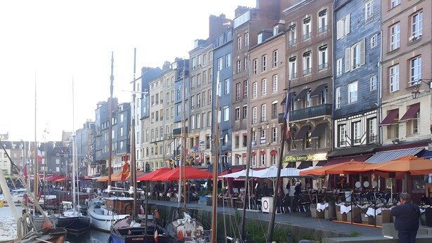 A marina with boats docked, a cobblestone waterfront, and buildings with outdoor seating. - Le cottage d'Honfleur, apartment with parking! (Honfleur)