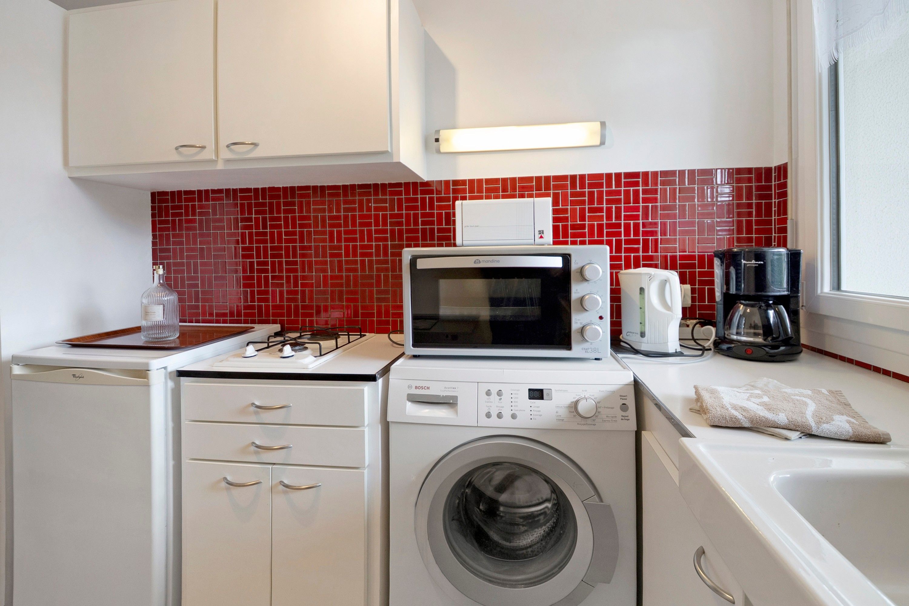 A compact kitchen with a microwave, coffee maker, and washing machine.