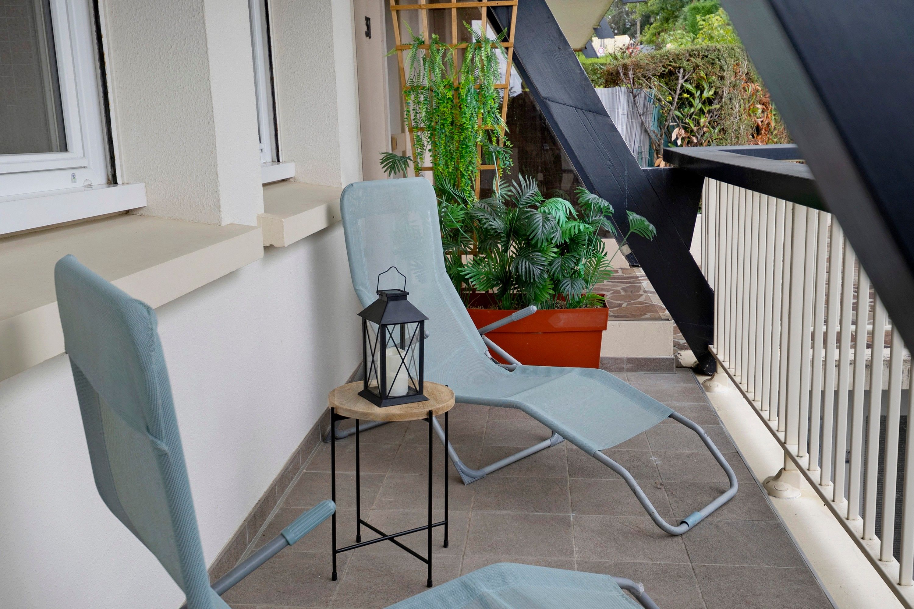 Un balcon avec une chaise, une petite table et un pot de fleurs.